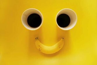 smiling face two paper cups coffee with banana yellow background 1 1